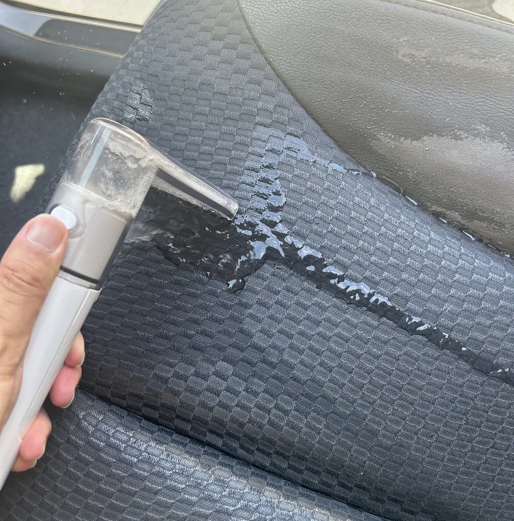 車のシートにリンサークリーナーのノズルを当てて汚れを吸い取っているところ